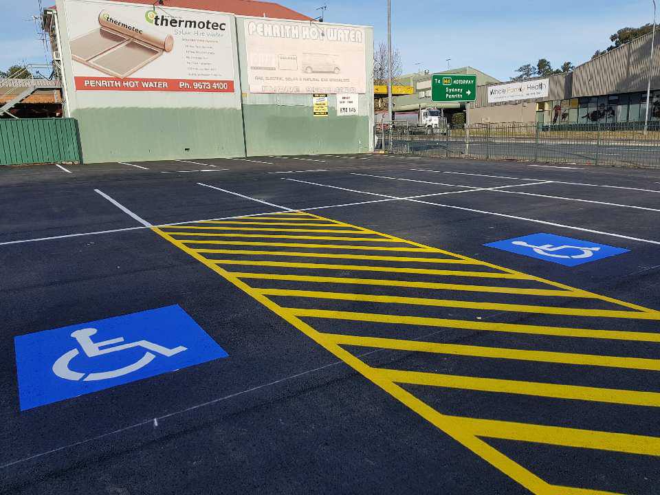 Two blue handicap parking symbols on a black pavement with yellow striped lines.