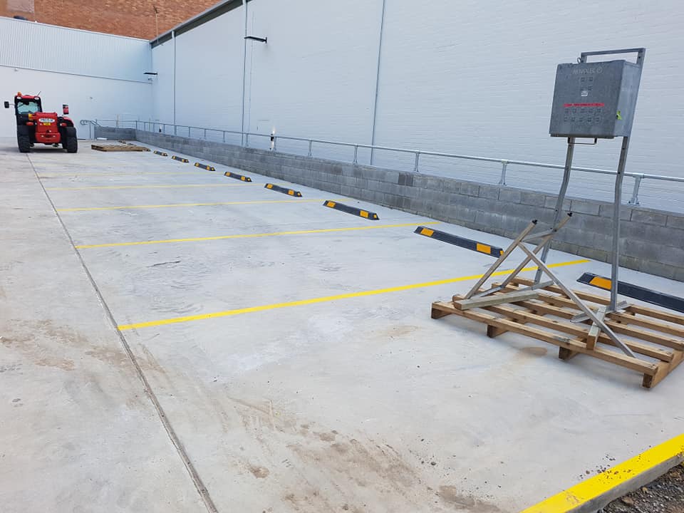 A parking lot with yellow stripes and black bumpers, a tractor parked on the left, and equipment on a wooden pallet.