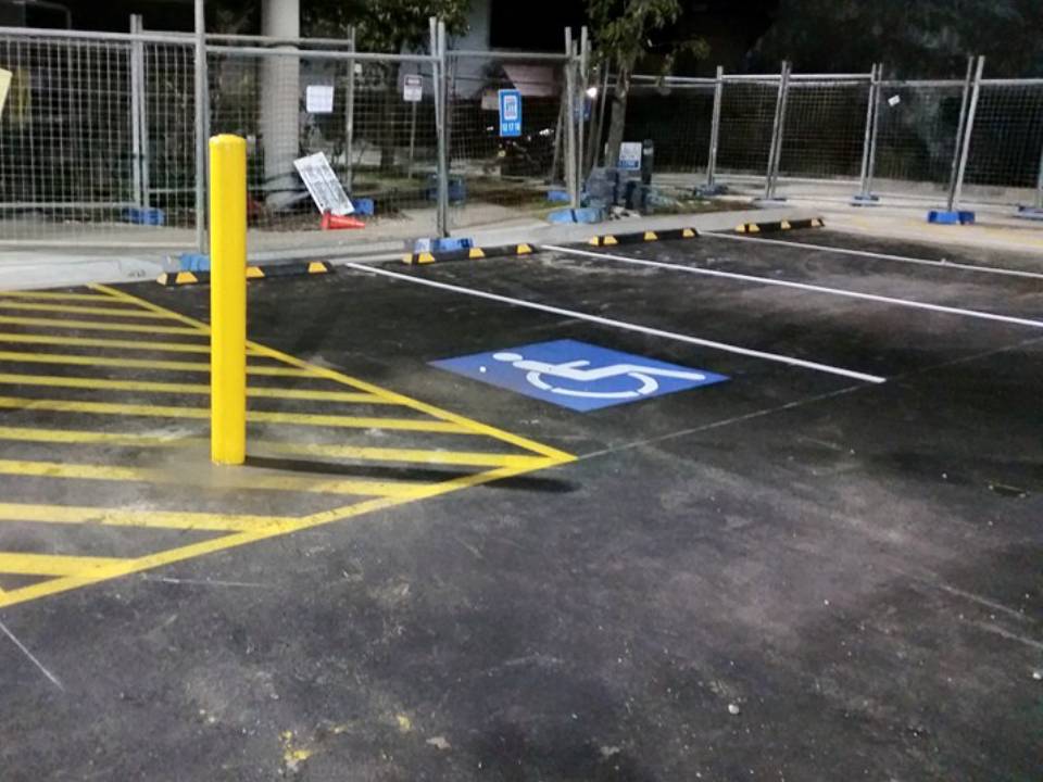 A parking lot at night with a yellow post and a blue handicapped parking sign on the ground.
