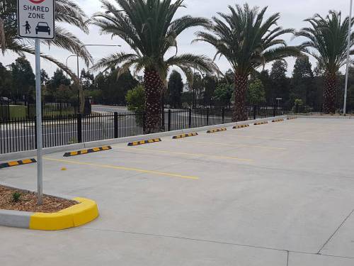 A parking lot with yellow and black curb markers, palm trees, and a shared zone sign.
